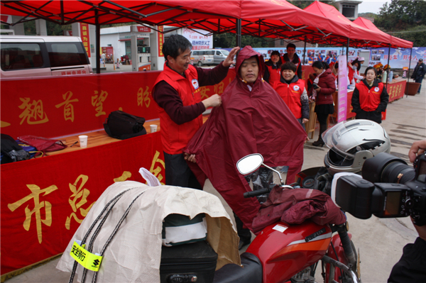 梧州市總工會的黨員義工們在市東出口春運(yùn)服務(wù)站助力“摩托大軍”平安返鄉(xiāng)，幫助他們檢查車輛和行李，穿上雨衣。--黃賀峰攝.j